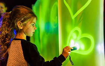 Girl with flashlight drawing on green lit up wall