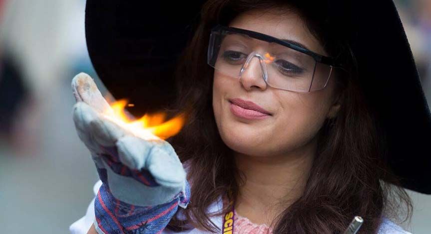 A female mad Scientist wearing a black hat holding fire in her hand