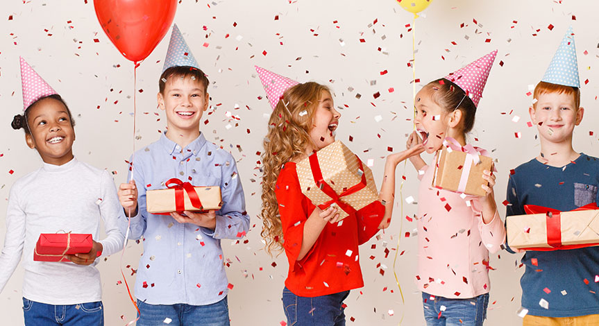 Kids celebrating birthday holding balloons and presents wearing birthday hats with confetti falling over white background
