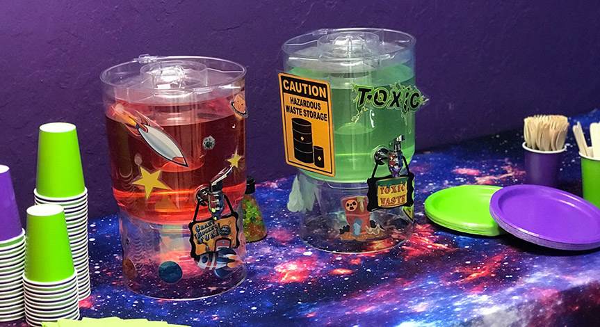 A mad science party table with spooky green and red juice and purple and green cups and plates.