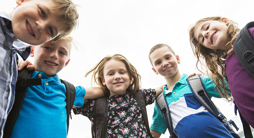 Kids looking down with arms around each all wearing school bags