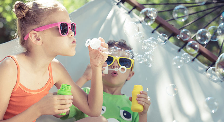 Two happy children wearing sunglasses lie on a hammock and play with soap bubbles