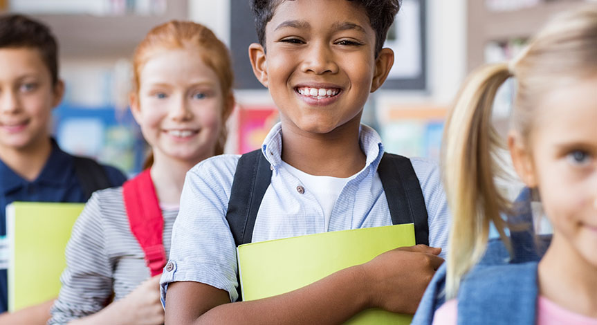 School children standing in a row holding notebooks wearing school bags