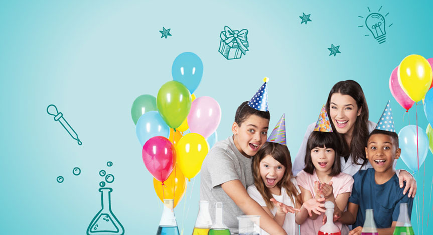 4 kids celebrating a birthday party with balloons and birthday hats.  Female scientist smiling in back of children 