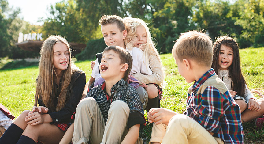 A group of happy smiling children sitting on the green grass in the park.